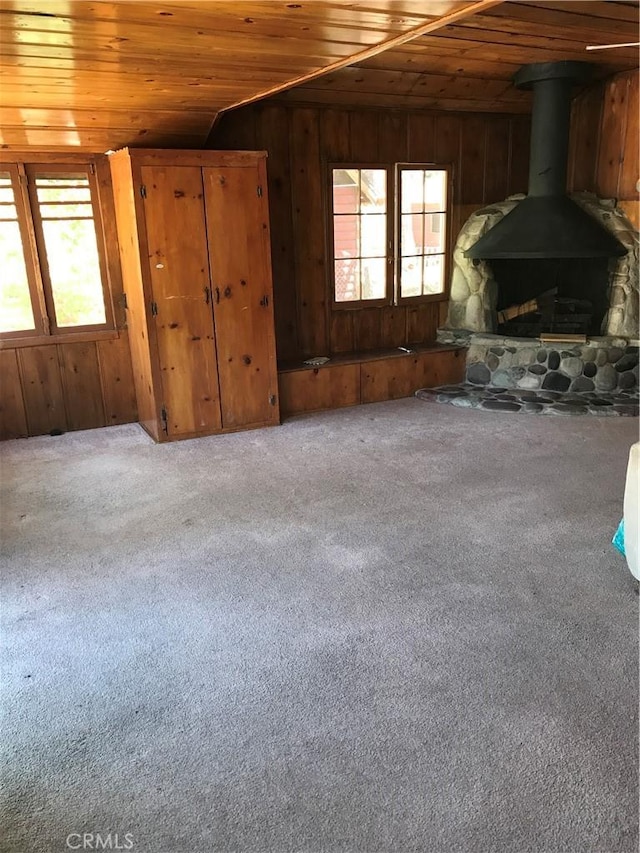 unfurnished living room with wood ceiling, wooden walls, carpet flooring, vaulted ceiling, and a wood stove