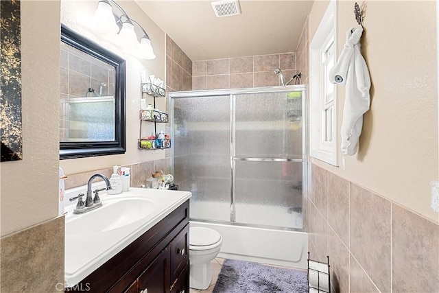 full bathroom featuring combined bath / shower with glass door, tile walls, vanity, tile patterned floors, and toilet