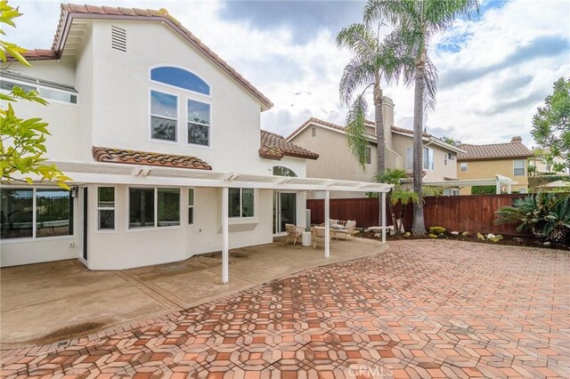 rear view of property featuring a tile roof, fence, a pergola, and stucco siding