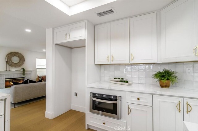 kitchen with light wood-type flooring, visible vents, a glass covered fireplace, and white cabinetry