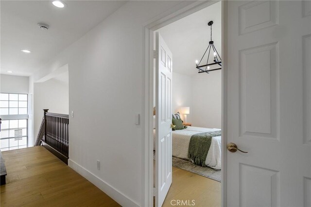 hall featuring baseboards, light wood finished floors, an inviting chandelier, recessed lighting, and an upstairs landing