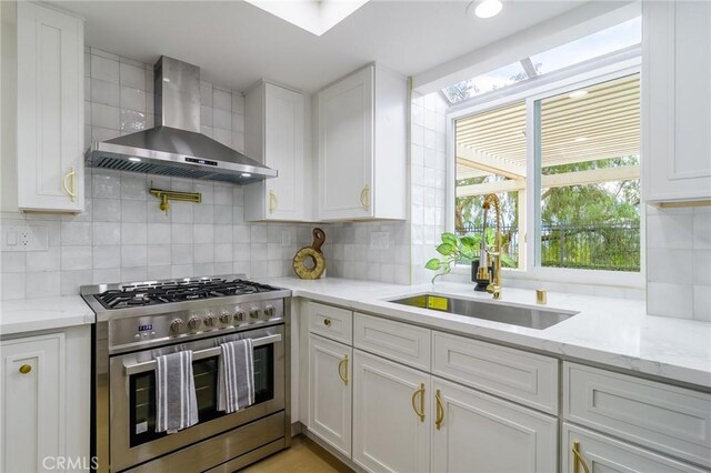 kitchen featuring a sink, tasteful backsplash, stainless steel stove, wall chimney exhaust hood, and white cabinets