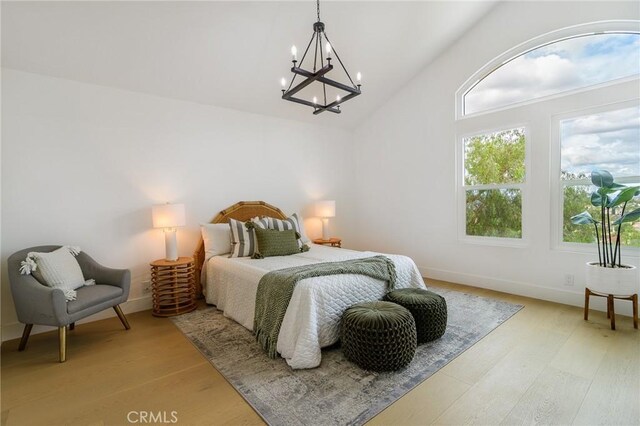 bedroom with baseboards, a notable chandelier, light wood-style flooring, and vaulted ceiling