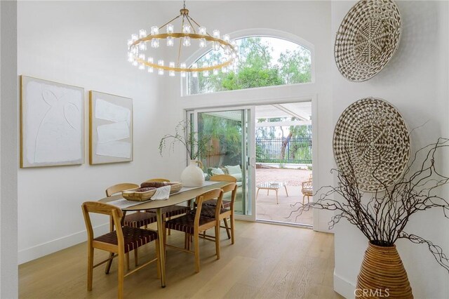 dining space with light wood finished floors, a notable chandelier, baseboards, and a towering ceiling