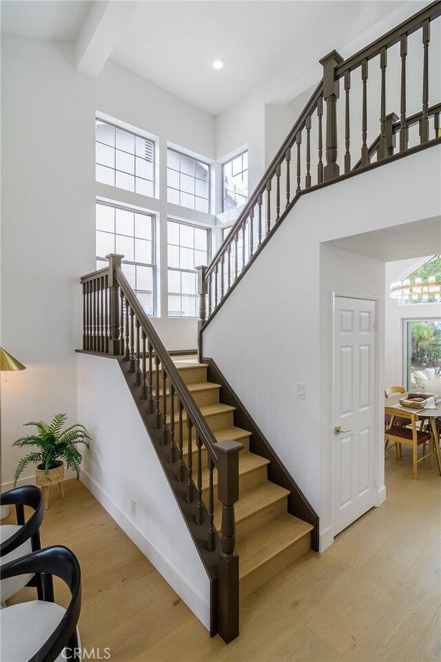 stairway featuring beam ceiling, a high ceiling, a healthy amount of sunlight, and wood finished floors