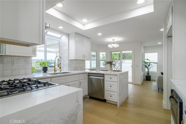 kitchen with a peninsula, light wood-style flooring, stainless steel appliances, decorative backsplash, and white cabinets