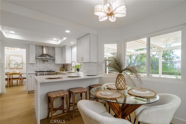 kitchen with light wood finished floors, backsplash, light countertops, wall chimney exhaust hood, and a sink