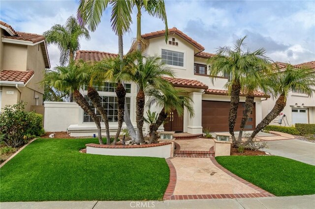 mediterranean / spanish house with stucco siding, concrete driveway, a front lawn, and a tiled roof