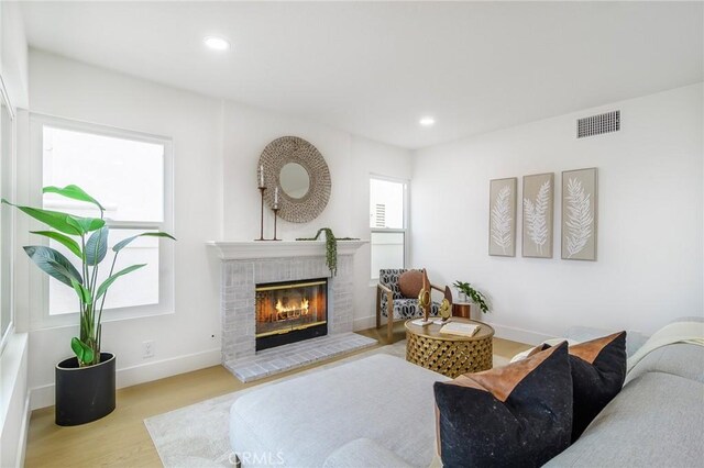 living area featuring wood finished floors, visible vents, baseboards, recessed lighting, and a brick fireplace