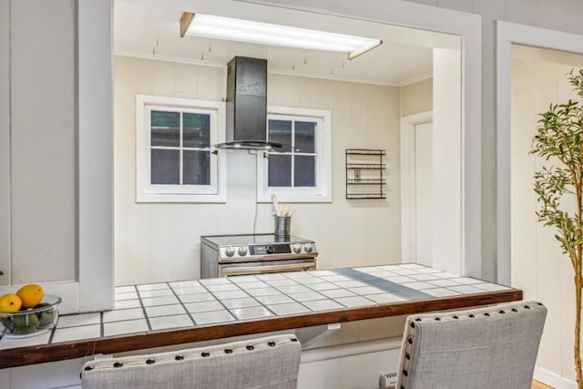 interior space with electric stove, wooden walls, ornamental molding, tile countertops, and exhaust hood