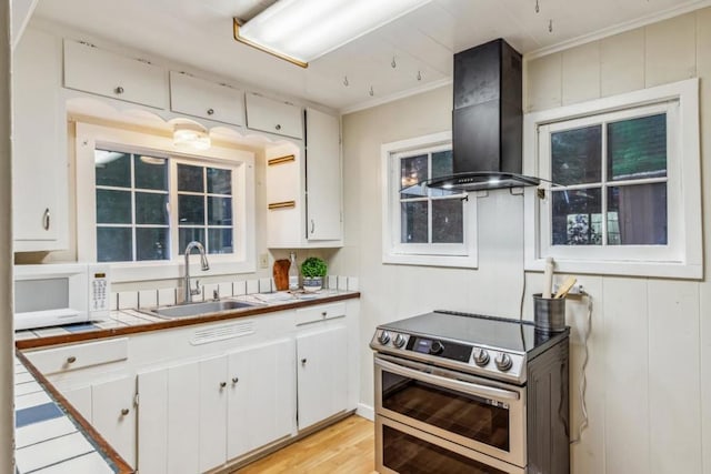 kitchen featuring tile countertops, range hood, white cabinetry, sink, and range with two ovens