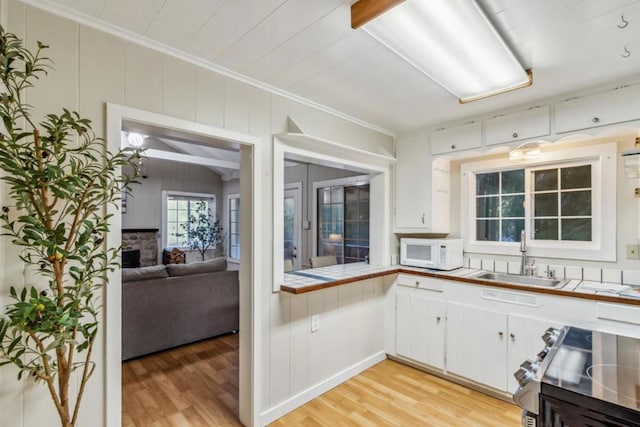 kitchen featuring sink, light hardwood / wood-style flooring, stainless steel range, white cabinets, and tile countertops