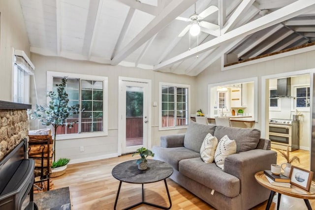 sunroom / solarium featuring ceiling fan, a stone fireplace, and lofted ceiling with beams