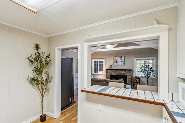 kitchen with tile counters, stainless steel fridge, a fireplace, and light hardwood / wood-style flooring