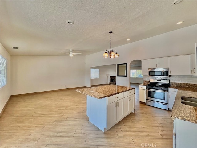 kitchen featuring appliances with stainless steel finishes, white cabinetry, light hardwood / wood-style floors, a kitchen island, and decorative light fixtures