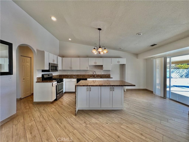 kitchen featuring white cabinetry, decorative light fixtures, an island with sink, stainless steel appliances, and light hardwood / wood-style floors