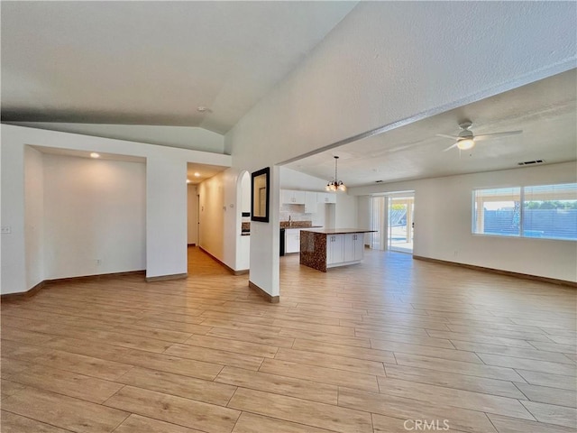 unfurnished living room with ceiling fan with notable chandelier, vaulted ceiling, and light wood-type flooring