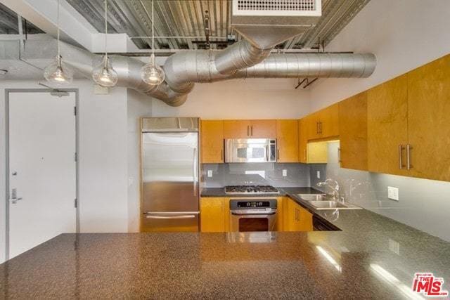 kitchen featuring sink, stainless steel appliances, a high ceiling, tasteful backsplash, and decorative light fixtures