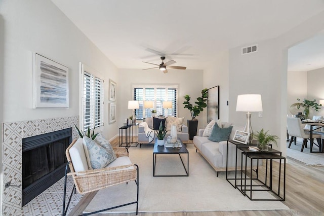 living room featuring ceiling fan, a tile fireplace, and light hardwood / wood-style flooring