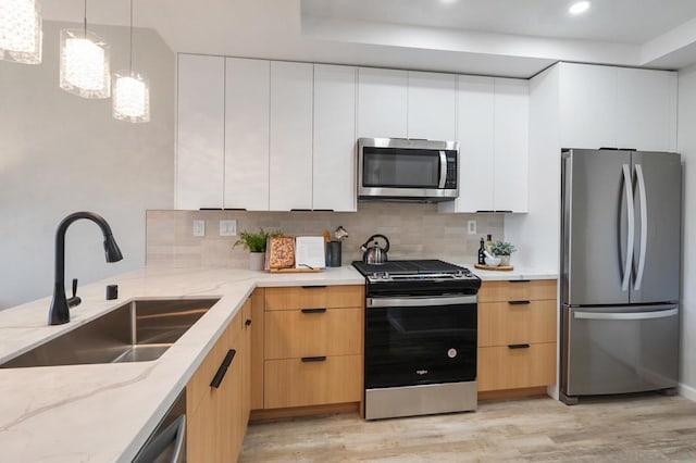 kitchen with sink, appliances with stainless steel finishes, decorative backsplash, white cabinets, and decorative light fixtures