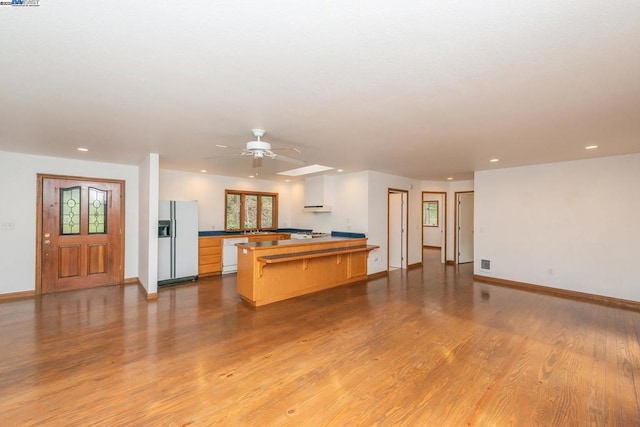 kitchen with a kitchen bar, white appliances, kitchen peninsula, ceiling fan, and light hardwood / wood-style floors