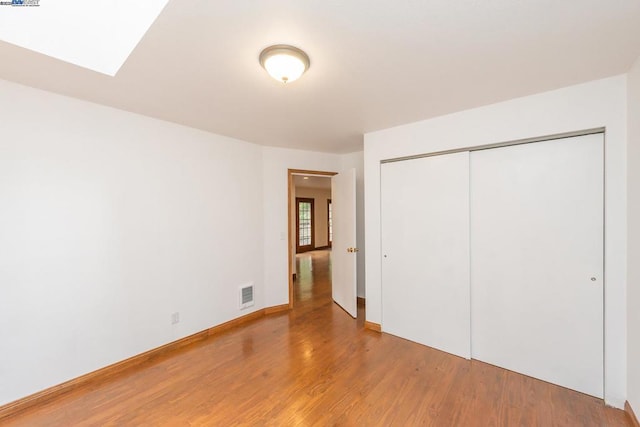 unfurnished bedroom with a skylight, wood-type flooring, and a closet