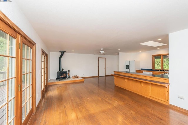 interior space featuring stainless steel refrigerator with ice dispenser, sink, a skylight, light hardwood / wood-style flooring, and a wood stove