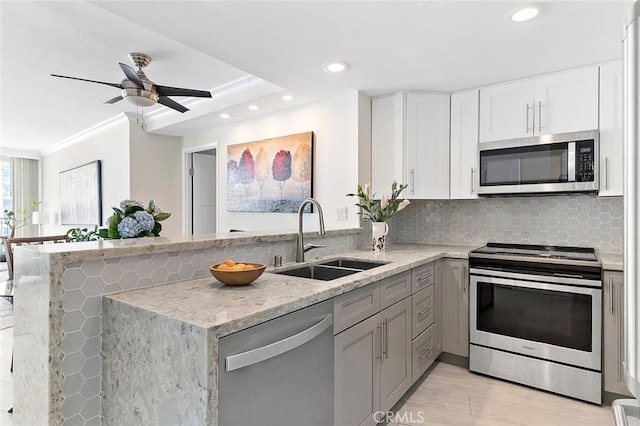 kitchen with sink, stainless steel appliances, light stone countertops, white cabinets, and kitchen peninsula