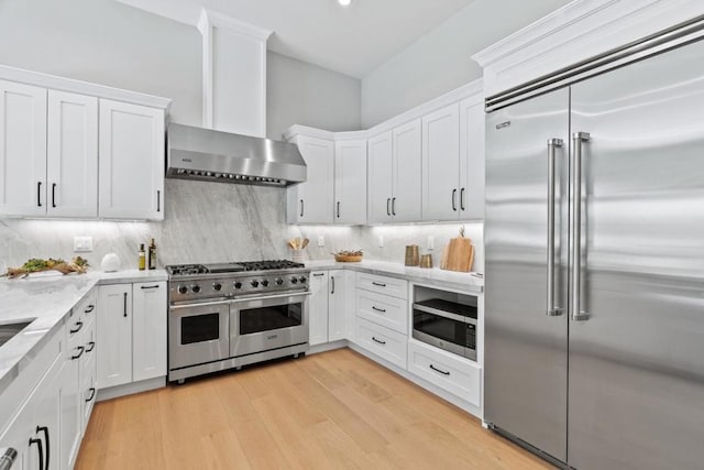 kitchen featuring white cabinetry, backsplash, built in appliances, light hardwood / wood-style floors, and light stone countertops