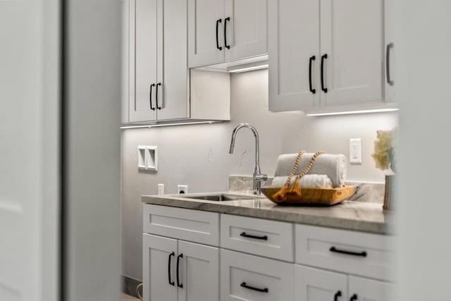 interior space featuring white cabinetry, light stone countertops, and sink