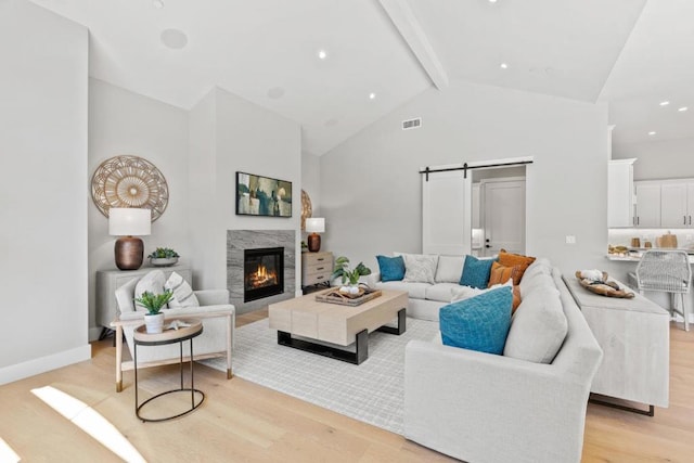 living room featuring a fireplace, a barn door, light hardwood / wood-style floors, and beam ceiling