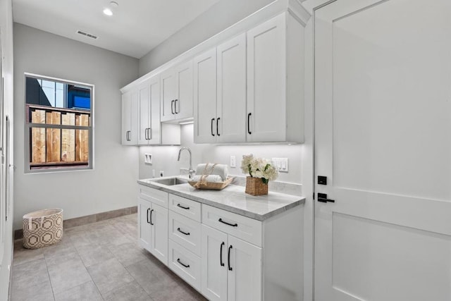 bar featuring sink, white cabinets, and light stone counters