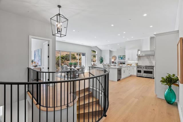 kitchen featuring wall chimney exhaust hood, white cabinetry, hanging light fixtures, stainless steel appliances, and backsplash