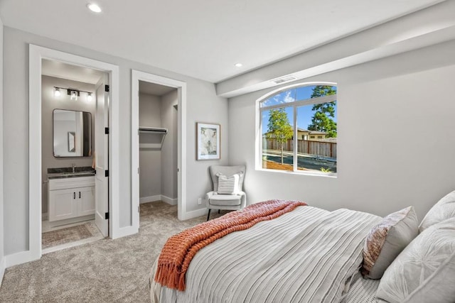 carpeted bedroom featuring a walk in closet, sink, a closet, and ensuite bath