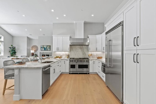 kitchen featuring wall chimney exhaust hood, a breakfast bar, sink, high quality appliances, and backsplash