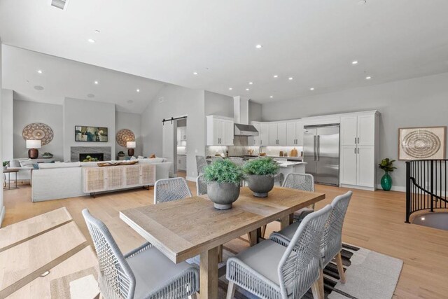 dining area with high vaulted ceiling, light hardwood / wood-style floors, and a barn door