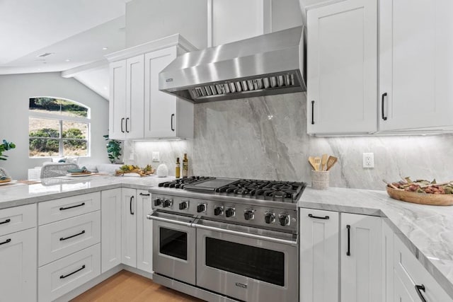 kitchen with lofted ceiling, light stone counters, wall chimney range hood, range with two ovens, and white cabinets