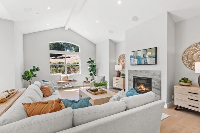 living room with a high end fireplace, light hardwood / wood-style floors, and vaulted ceiling with beams