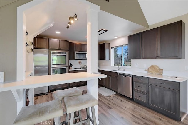 kitchen with vaulted ceiling, sink, a kitchen bar, light hardwood / wood-style floors, and stainless steel appliances