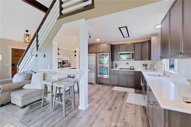 kitchen with sink, stainless steel appliances, light hardwood / wood-style floors, a kitchen bar, and beamed ceiling