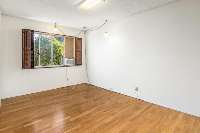 unfurnished room with cooling unit, hardwood / wood-style floors, and a textured ceiling