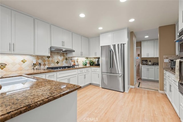 kitchen featuring appliances with stainless steel finishes, tasteful backsplash, white cabinetry, dark stone countertops, and light hardwood / wood-style flooring