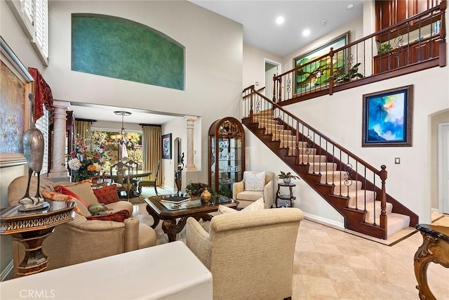 living room featuring an inviting chandelier, a towering ceiling, and ornate columns