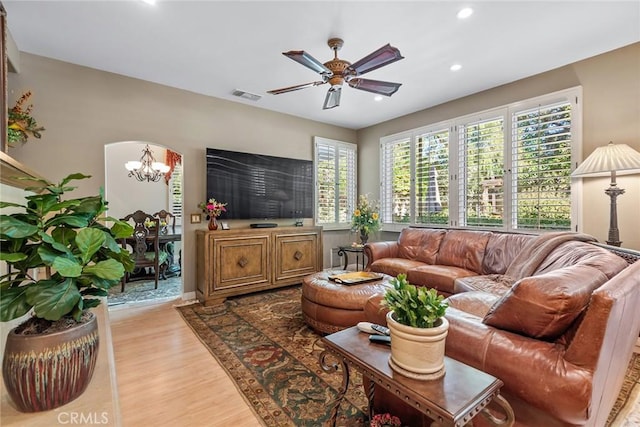 living room featuring ceiling fan with notable chandelier and light hardwood / wood-style flooring