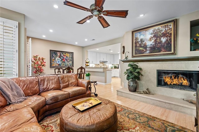 living room featuring ceiling fan, a fireplace, and light wood-type flooring