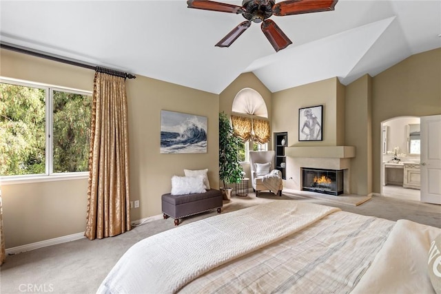 bedroom featuring light carpet, arched walkways, a glass covered fireplace, baseboards, and lofted ceiling