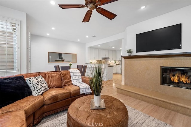 living room featuring recessed lighting, a ceiling fan, light wood-type flooring, and a high end fireplace