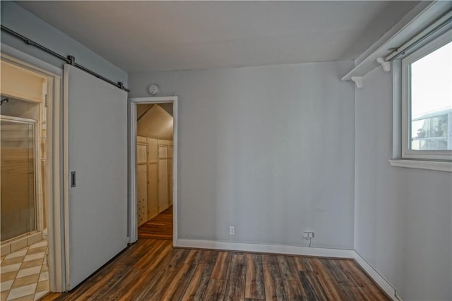 unfurnished bedroom featuring a barn door, dark hardwood / wood-style flooring, a closet, and a spacious closet