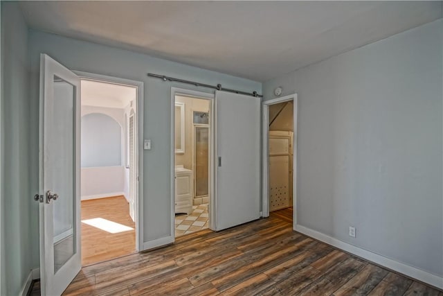 unfurnished bedroom with dark hardwood / wood-style floors, ensuite bath, and a barn door