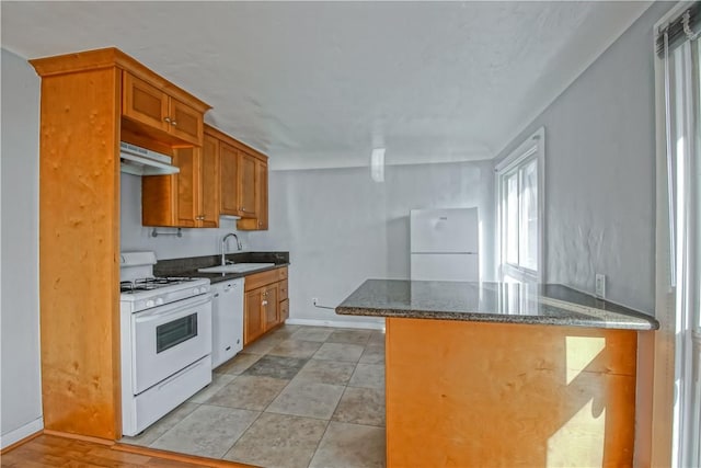 kitchen with white appliances, kitchen peninsula, sink, and dark stone countertops